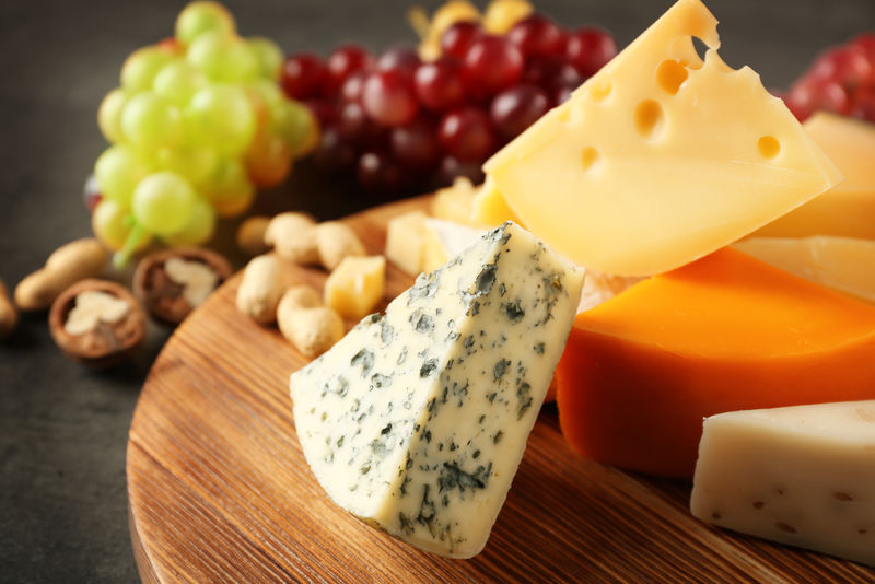 灰色背景下的奶酪、葡萄和坚果木板