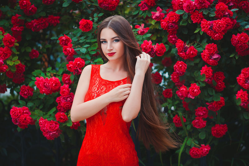 接近红玫瑰的性感黑发女郎的美丽画像