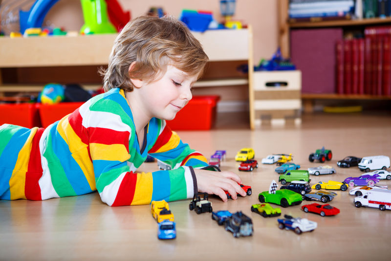 快乐有趣的小金发小孩在室内玩很多玩具车-男孩穿着彩色衬衫-在托儿所玩得很开心