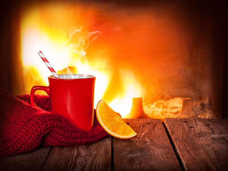红杯子里的热饮料和陈年木桌上的橘子片-以壁炉为背景-圣诞节或冬季暖饮-具有自由文本空间的布局