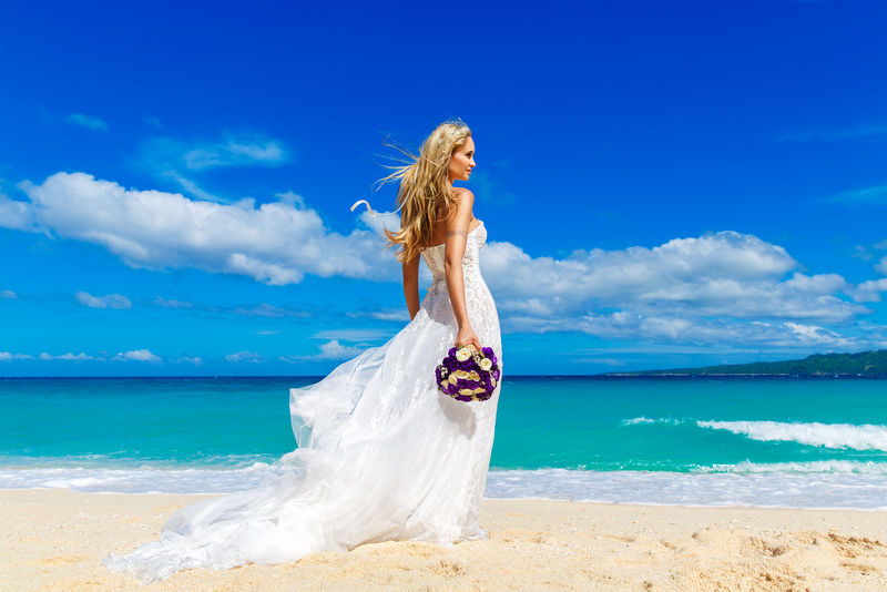 美丽的金发未婚妻-穿着白色婚纱-坐着长长的白色火车-在海边放着花束