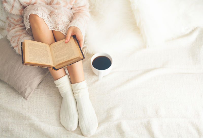 躺在床上的女人拿着一本旧书和一杯咖啡-俯视图