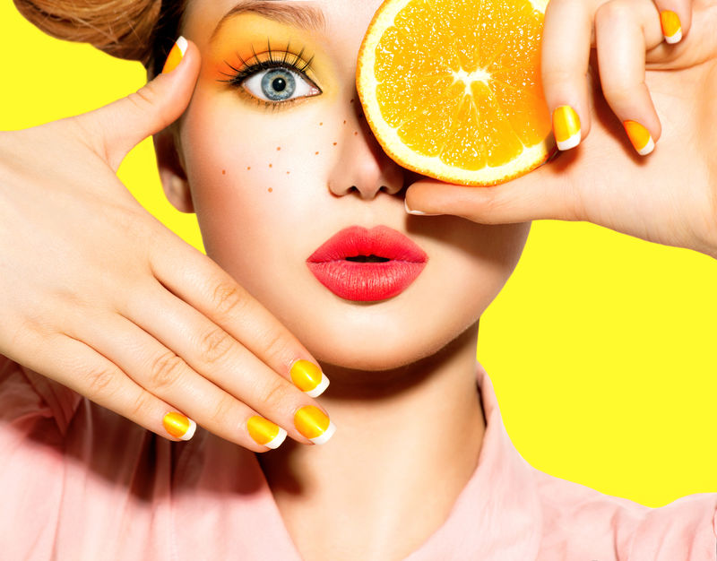 美女模特儿吃多汁的橙子-美丽快乐的少女有雀斑-有趣的红色发型-黄色化妆品和指甲-专业化妆-橘子片