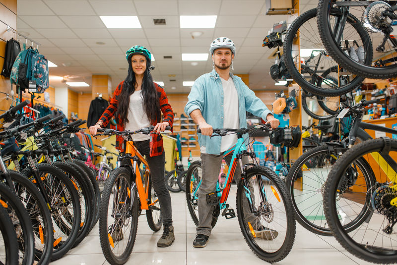 戴头盔的情侣在运动商店选择自行车