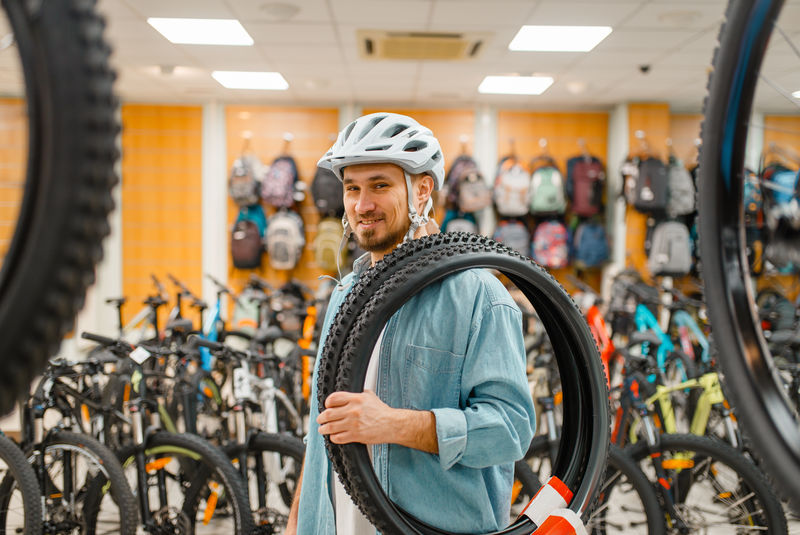 戴着自行车头盔的男人拿着自行车轮胎，购物