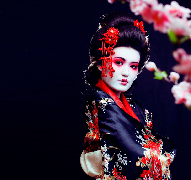 年轻漂亮的真正的艺妓穿着和服，带着樱花和装饰
