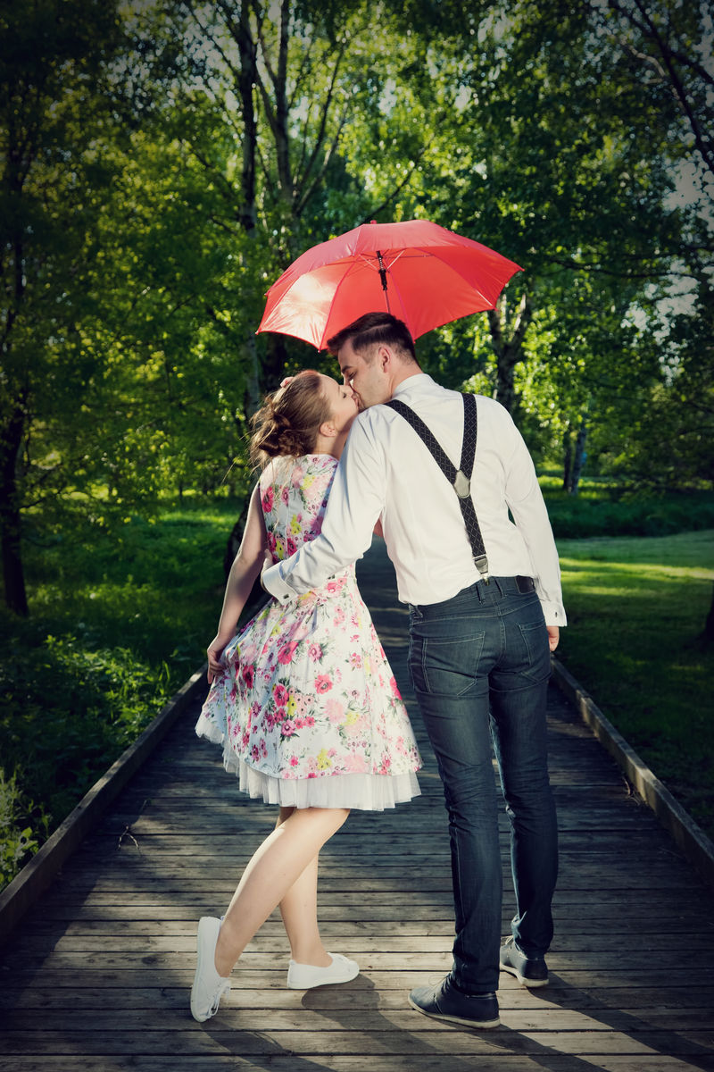 恋爱中的年轻浪漫情侣在雨中调情。红伞