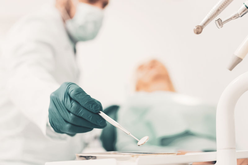 牙医用器械-老年妇女等待治疗时看台牙科器械和医生手持牙科反射镜的选择性聚焦
