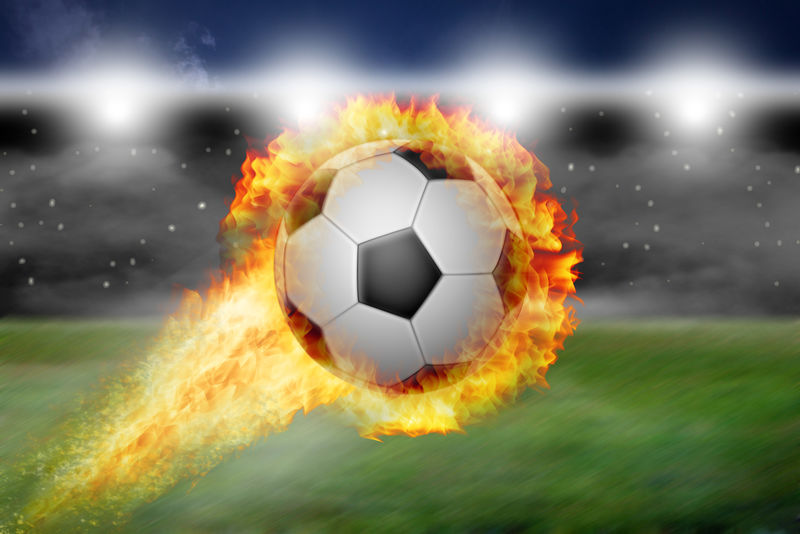 燃烧的足球飞过体育场的草坪-背景是带泛光灯的看台