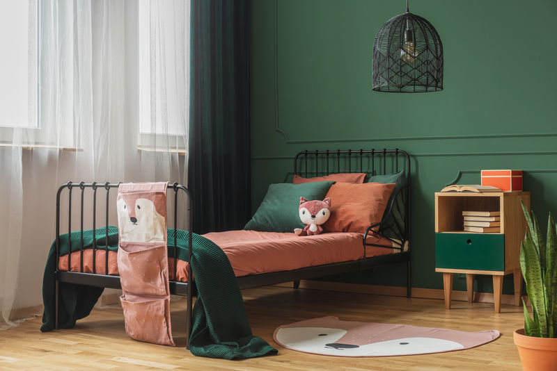 一张真实的照片，一块形状像狐狸的毯子躺在孩子卧室的木地板上，橙色的床单和枕头放在一张黑色的床上，靠着窗户