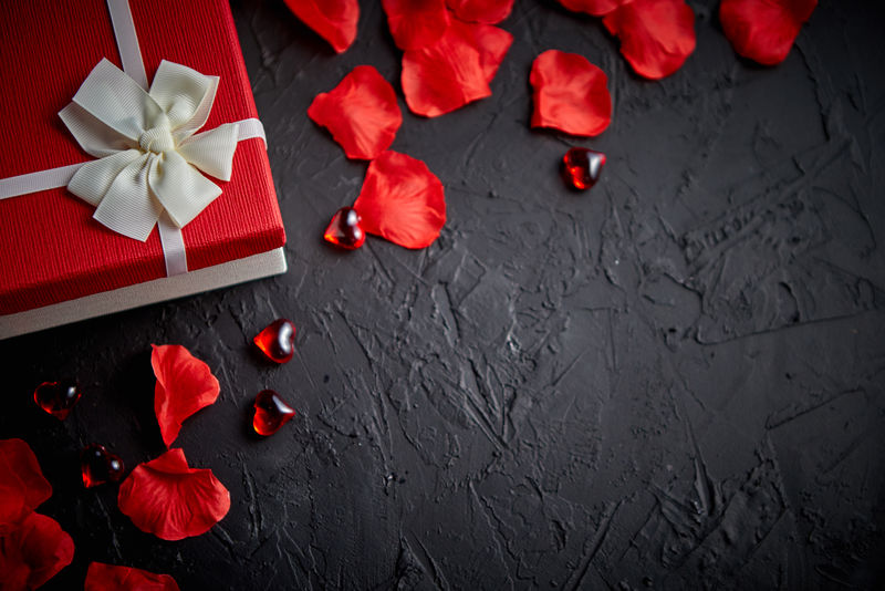 黑石桌上的礼品盒。带玫瑰花瓣的浪漫假日背景