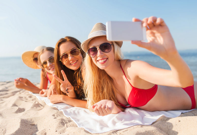 一群带着智能手机在海滩上微笑的女人