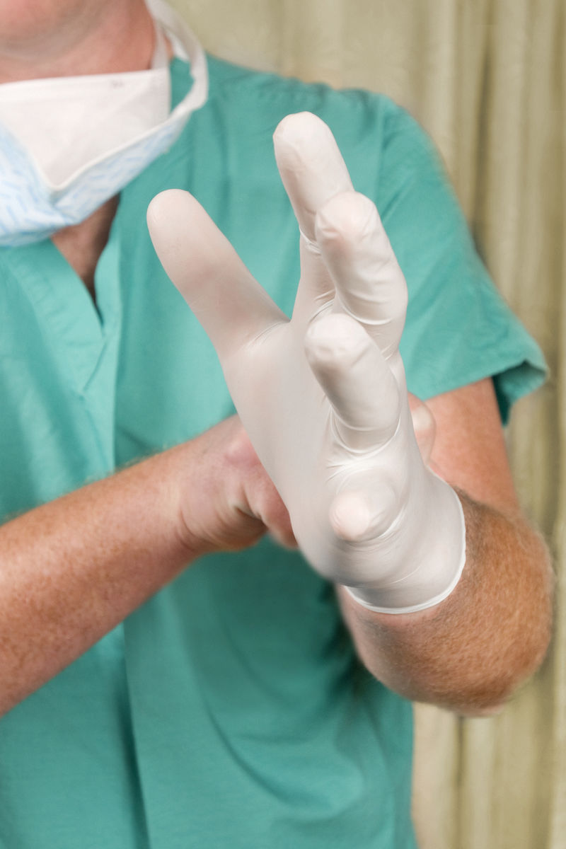 一位医疗保健提供者戴上一副绿色乳胶手套以便在接下来的互动中保护自己