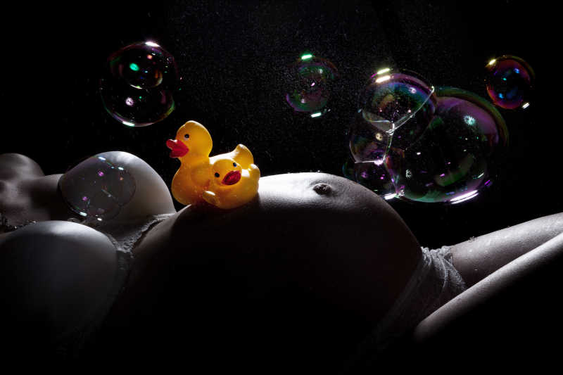 黑色背景下躺着的孕妇腹部的玩具小鸭