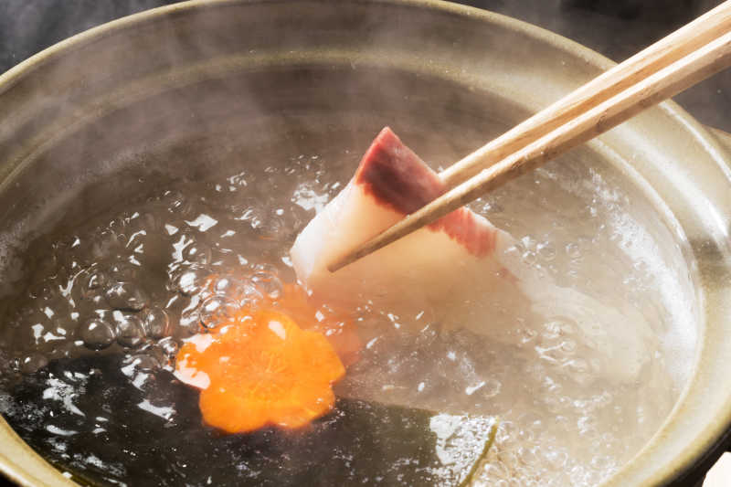 筷子夹起来的冒着热气的砂锅里的鱼片