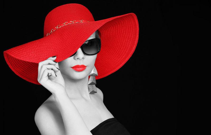 黑色背景下戴着红色的帽子和黑色的太阳眼镜的美女