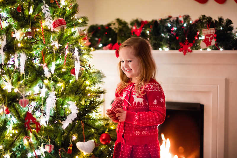 穿着红色毛衣的小女孩在圣诞树上挂装饰品