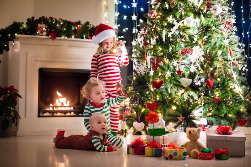 圣诞树下穿睡衣的孩子给婴儿玩耍