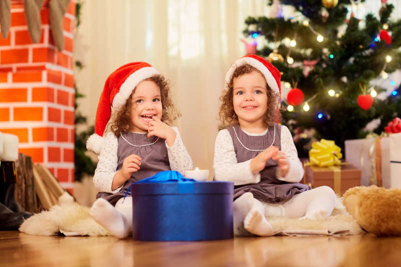 圣诞树边两个带着圣诞帽子额可爱小女孩