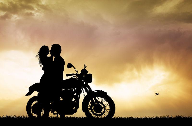 落日下坐在摩托车上接吻的夫妇
