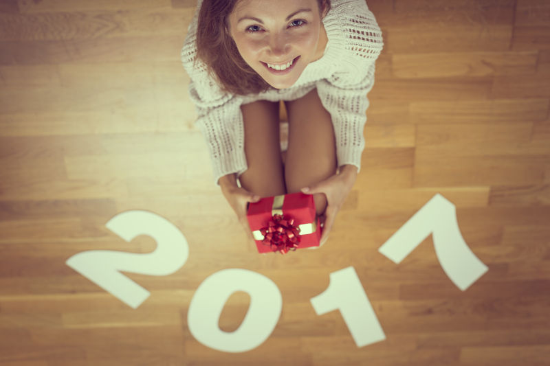 拿着圣诞礼物微笑的美女蹲在印有2017数字的地板上